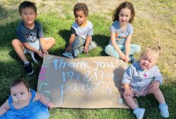 Five toddler and preschool aged children sitting on a sign that says 